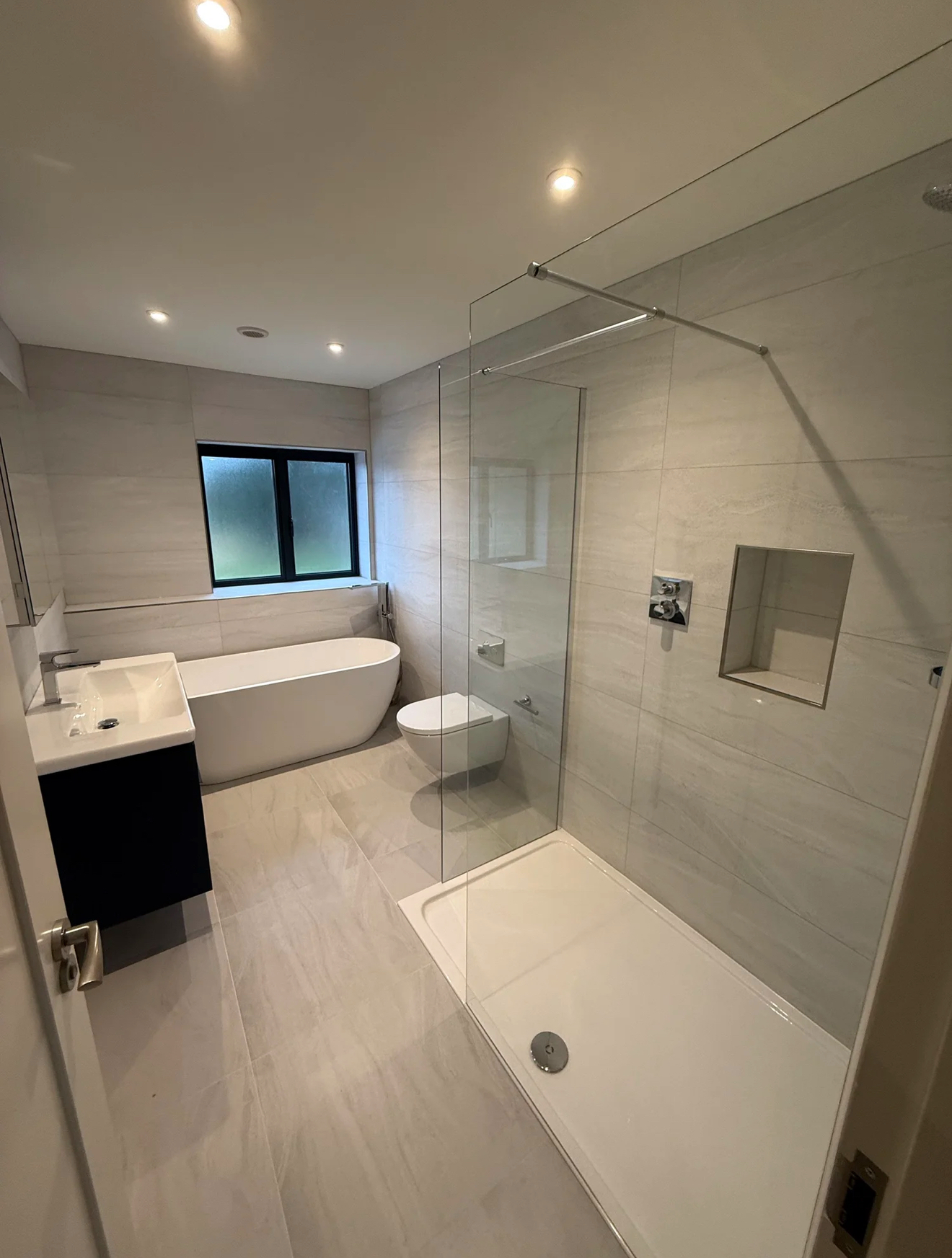 White marble family bathroom with freestanding bath and glass shower screen — bathroom fitters Basingstoke