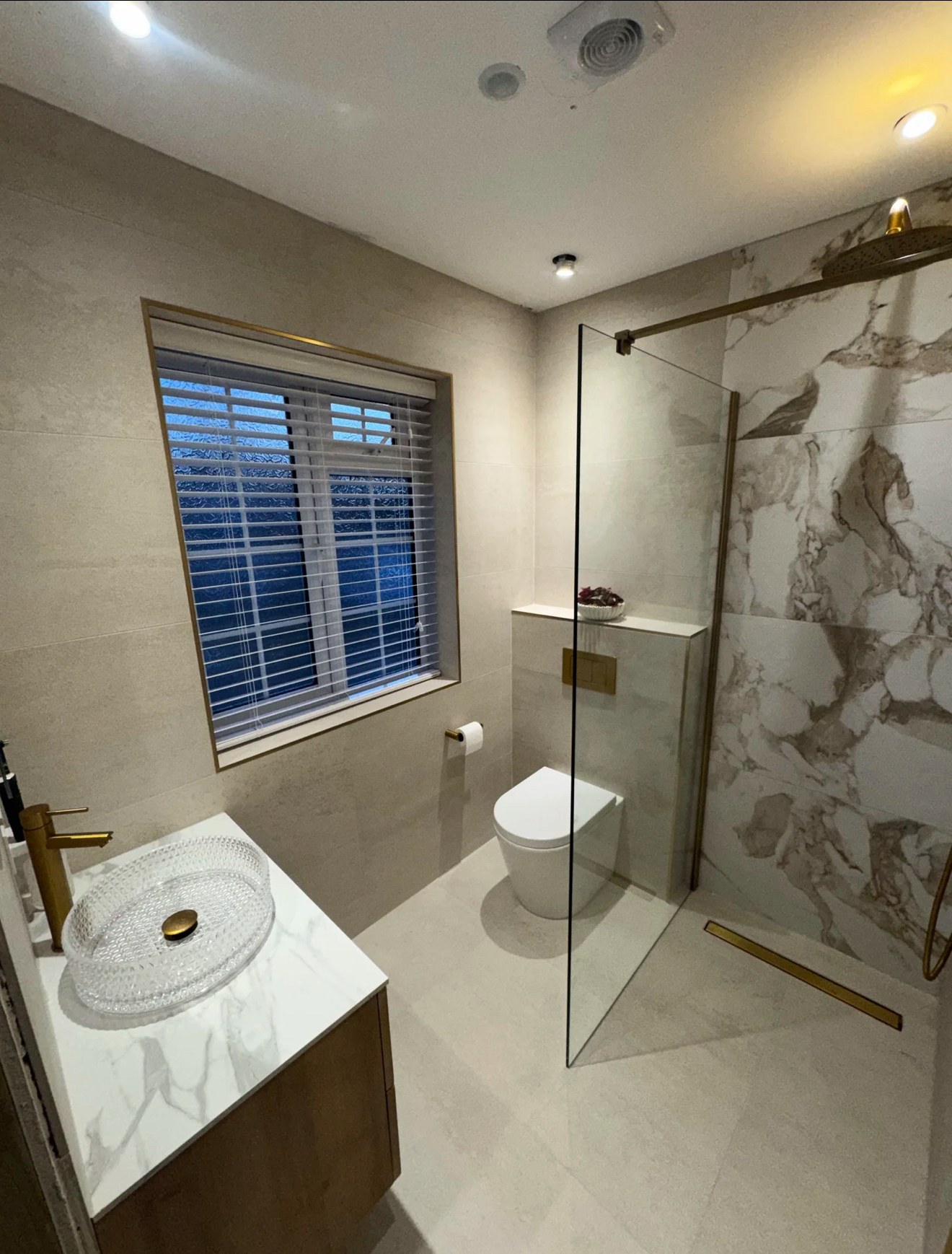 Brushed brass shower room with glass vessel basin and marble shower wall — bathroom fitters Basingstoke